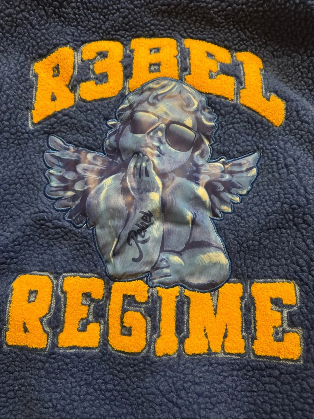 Soft  blue sherpa jacket with bold yellow 'Rebel Regime' lettering and angel